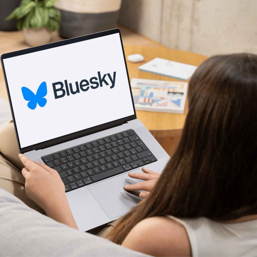 User holding a phone showing the Bluesky app interface for account creation. 